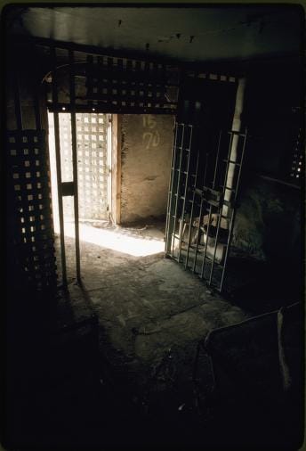 view through bars toward light from a darkened jail cell. the jail barred door is open